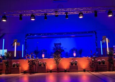 Scène événementielle intérieure avec structure en aluminium, éclairage LED bleu et orange, décor floral et plantes, ambiance professionnelle et moderne