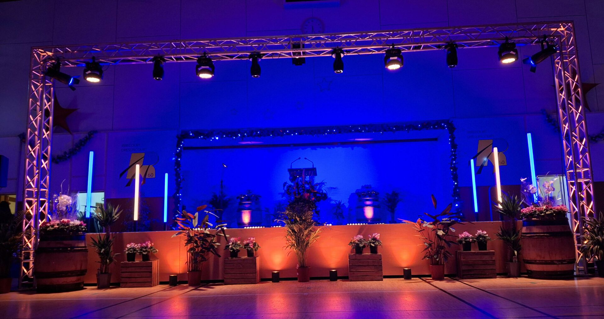 photo-lumière-site Scène événementielle intérieure avec structure en aluminium, éclairage LED bleu et orange, décor floral et plantes, ambiance professionnelle et moderne